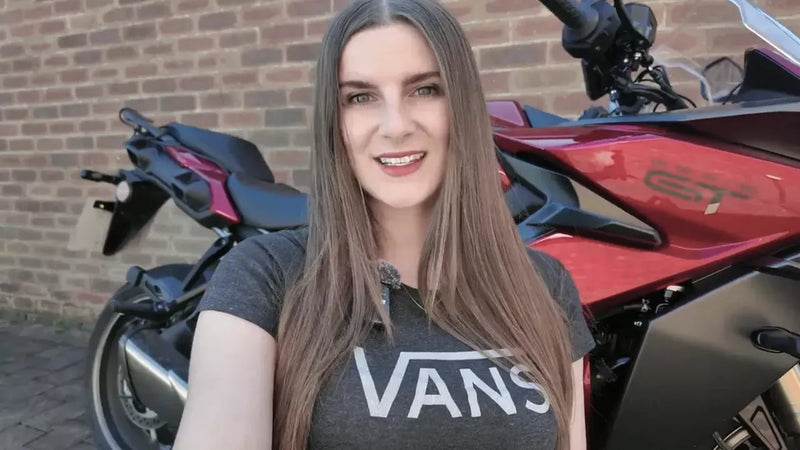 Person wearing a Vans shirt standing next to a red motorcycle with a brick wall background